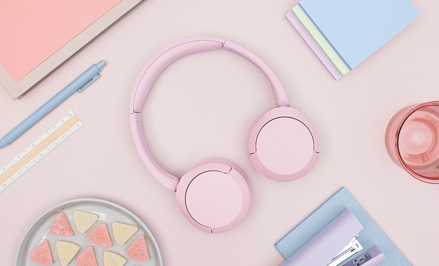 A pair of pink Sony WH-CH520 headphones on a pastel desk.